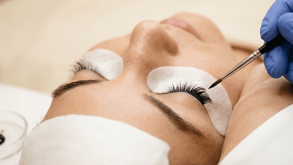 Close-up of eyelash treatment with under-eye pads and precision tool during a lash appointment