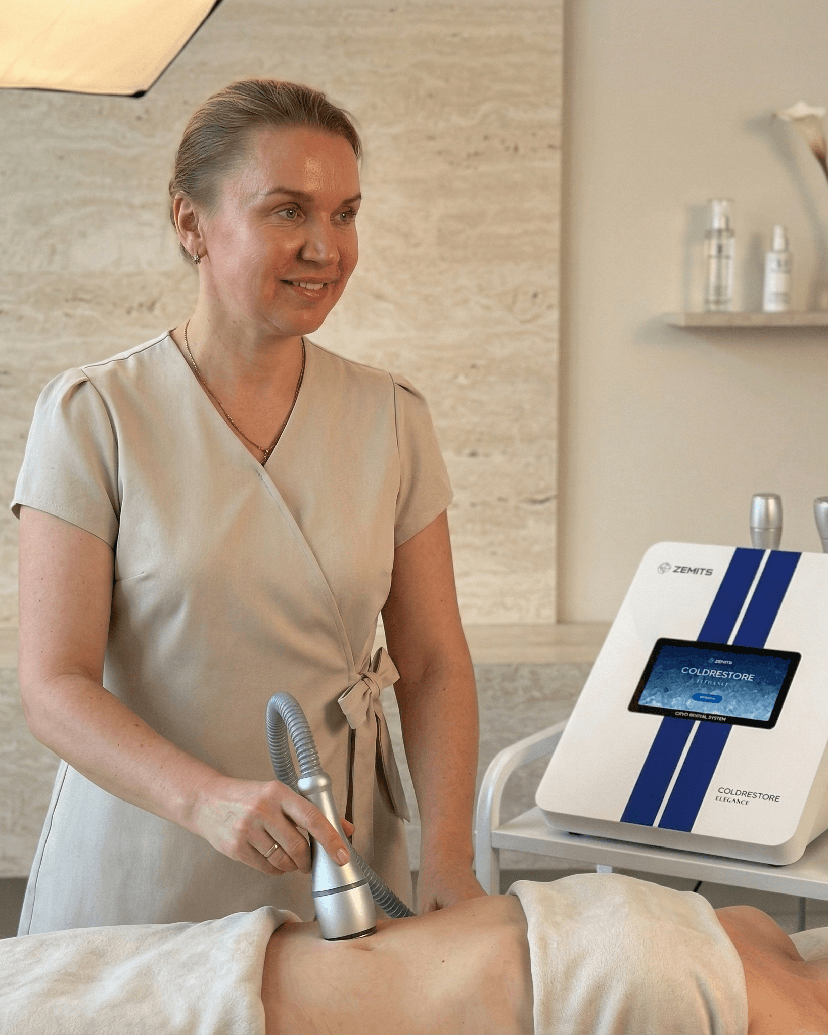 Therapist performing a non-invasive fat-freezing treatment with a handheld applicator on a client’s abdomen