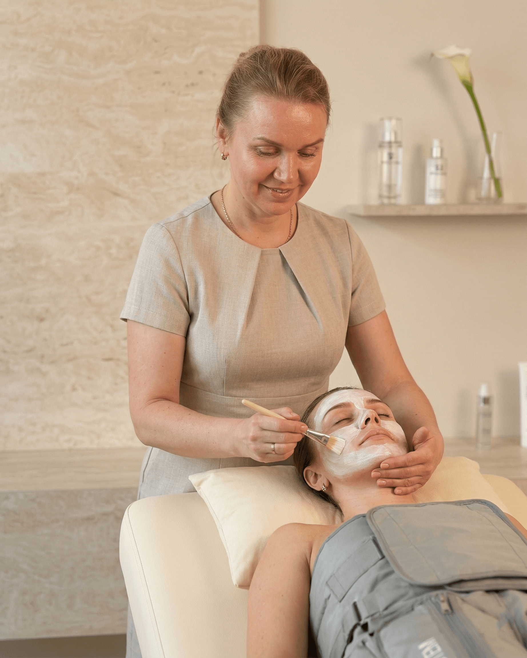 Maria - Therapist applying a facial mask while the client wears a pressotherapy suit during treatment