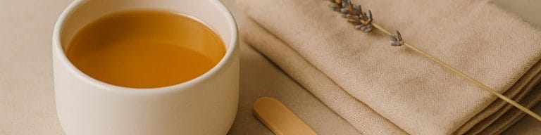 Honey wax pot, bamboo spatula, dried lavender on beige stone. Hollywood waxing. Skincare & Waxing Kirkham.